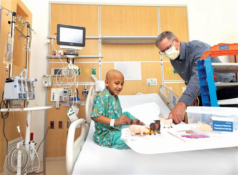 Photo of a patient in his hospital bed wearing scrubs and a chaplain playing with him.