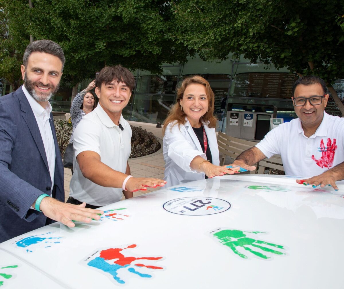 Hyundai Hope on Wheels representatives, patient Tyler, and Dr. Raya Saab stand in front of a Hyundai vehicle and place colorful handprints on the hood.
