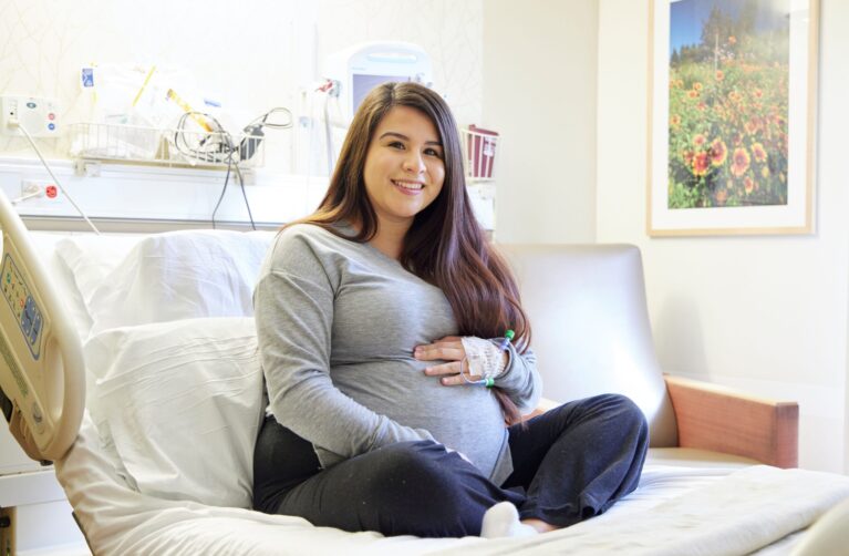 Pregnant woman seated on a hospital bed.