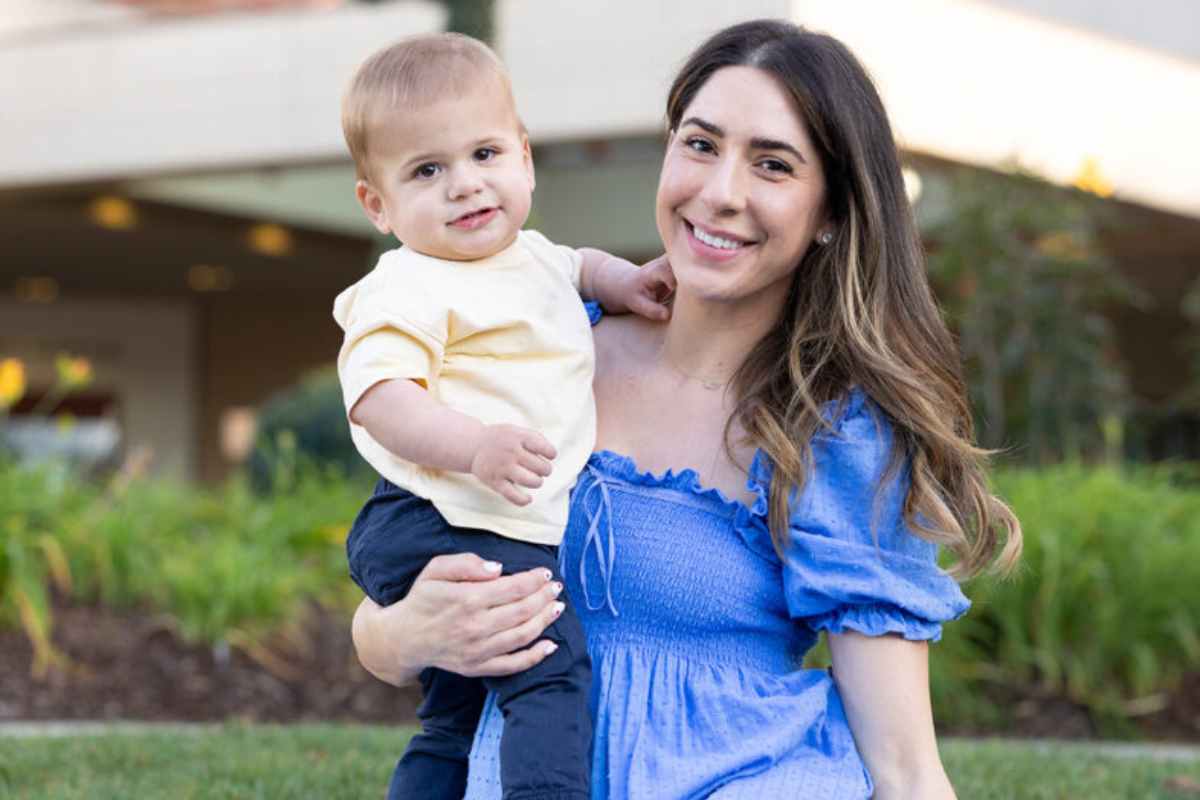 Former Packard Children's patients, parent and child, sitting in front of Packard Children's and smiling at the camera.