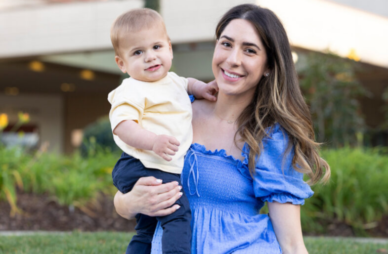 Former Packard Children's patients, parent and child, sitting in front of Packard Children's and smiling at the camera.
