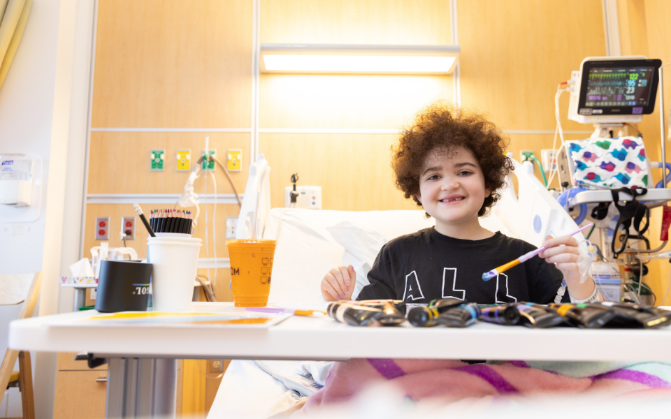 Pediatric patient engaged in art therapy, painting in a hospital bed and smiling in a bright, warm hospital room..