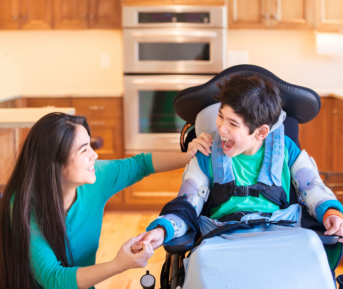 Nine year old disabled boy in wheelchair laughing with teen sister in kitchen