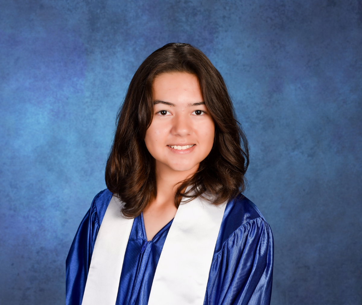 Portrait of a middle school graduate in a blue graduation gown and white stole seated against a dark blue backdrop and facing the camera.