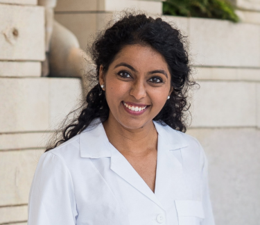 Pediatric physician-scientist smiling in a white lab coat outside Lucile Packard Children's Hospital Stanford.