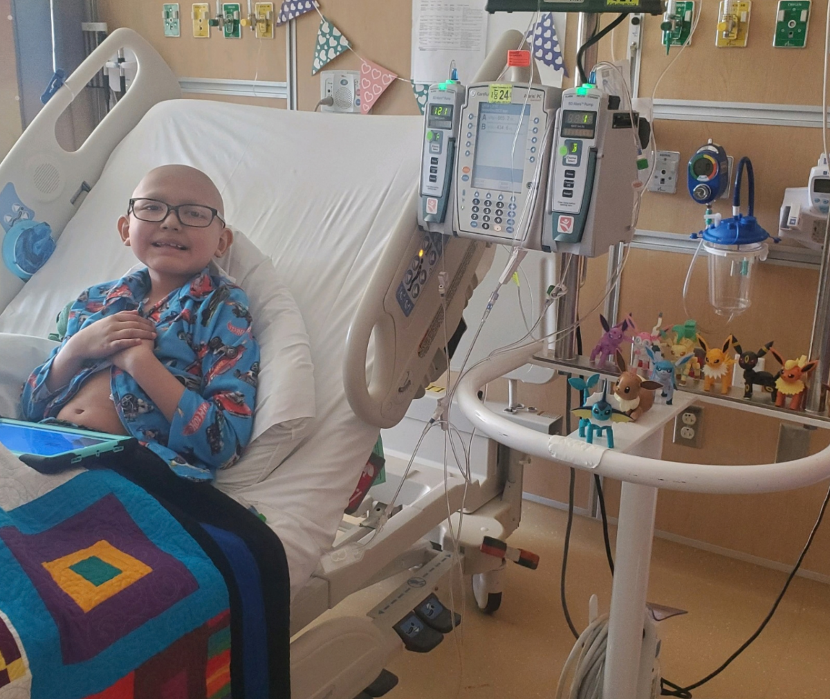 Lucile Packard Children's Hospital Stanford patient Josh wears a hospital gown and sits up right in a hospital bed. Josh smiles at the camera.