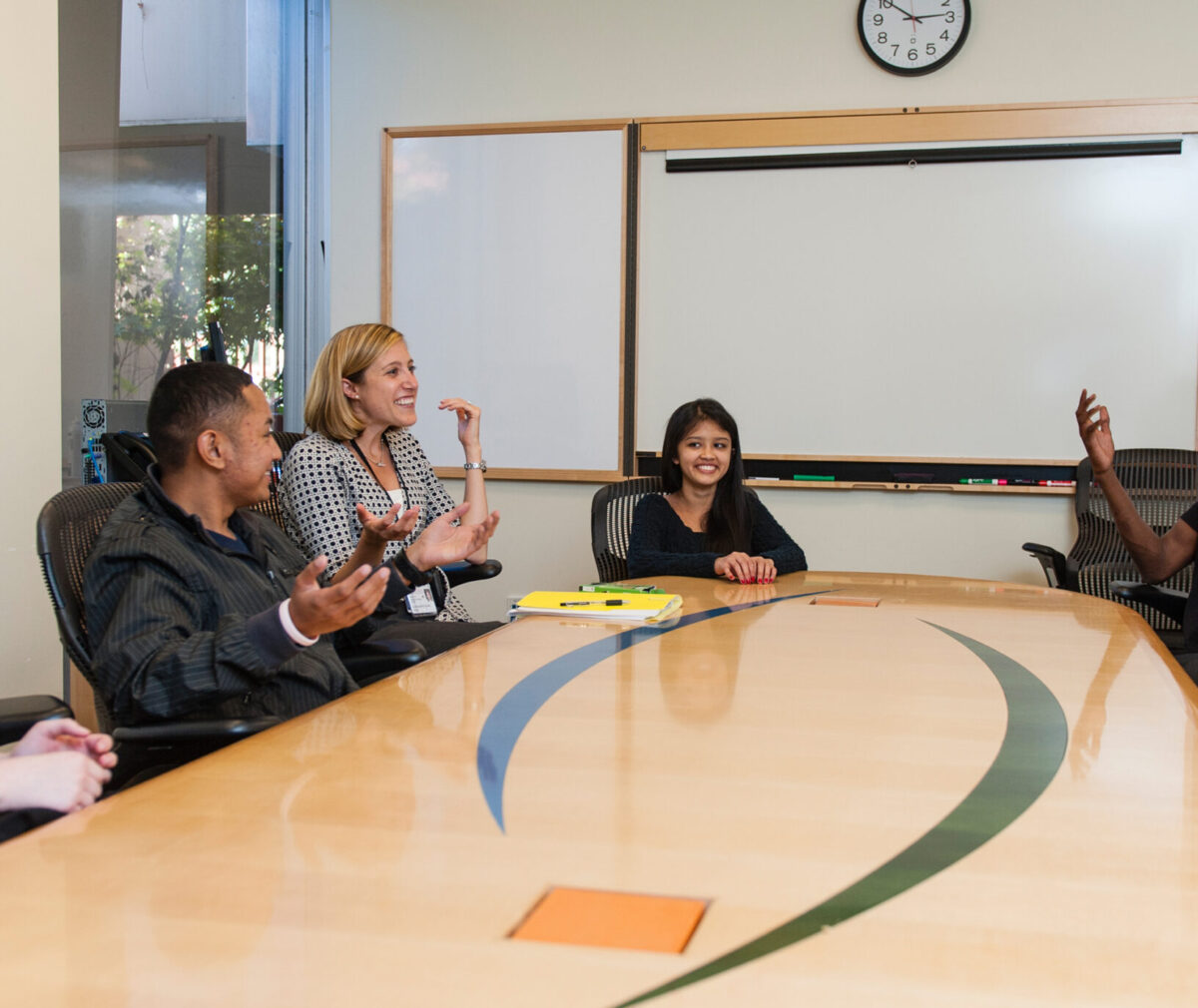 LaJay Phillips sitting and talking at a conference table with three smiling teenagers.