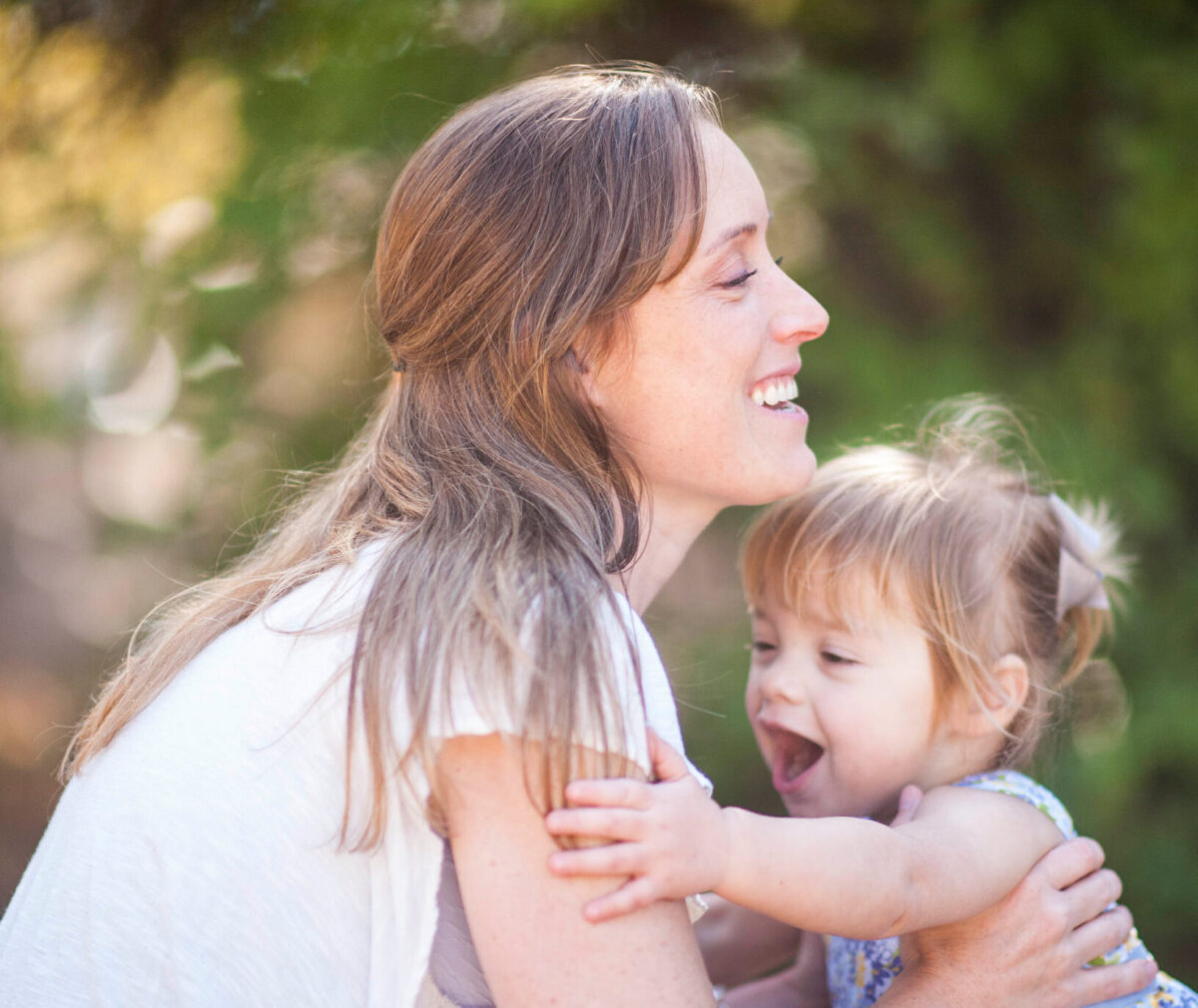 A mother bends down to pick up a toddler that is running into her arms.