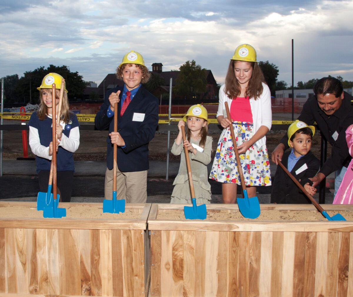 A group of kids wearing yellow hardhats and holding shovels pose for a picture at the groundbreaking of the lucile packard children's hospital's expansion.
