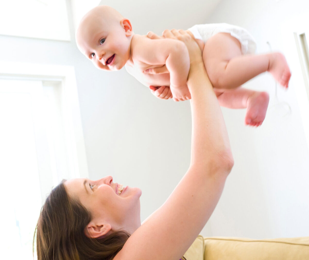 A mom holds her baby up in the air over her head. The baby is smiling and only wearing a diaper.