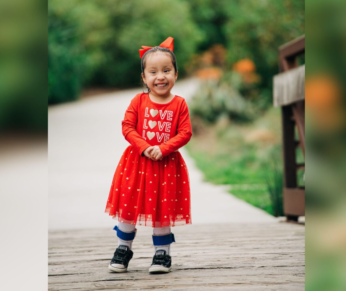 Iliana in red dress smiling at camera on a bridge.
