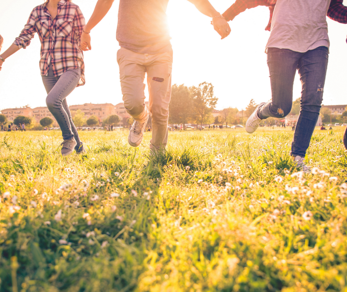Stock image of group of adults running in grass with sun shinning behind.