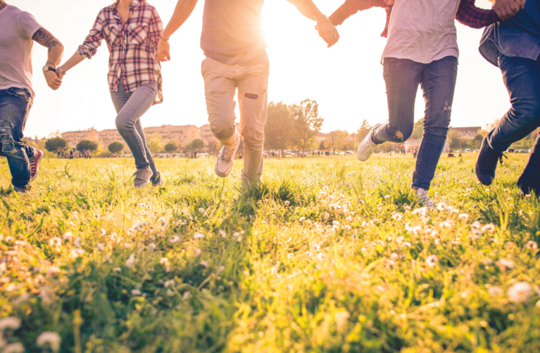 Stock image of group of adults running in grass with sun shinning behind.