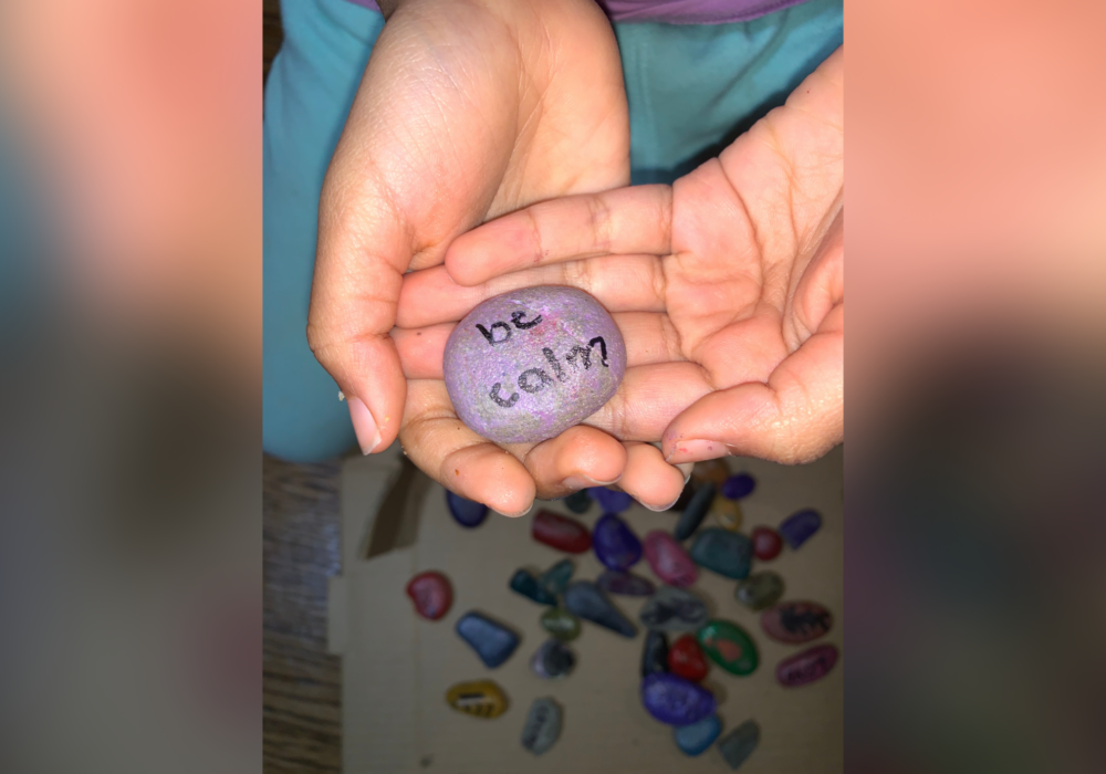 Hands holding a painted rock with be calm written on it.