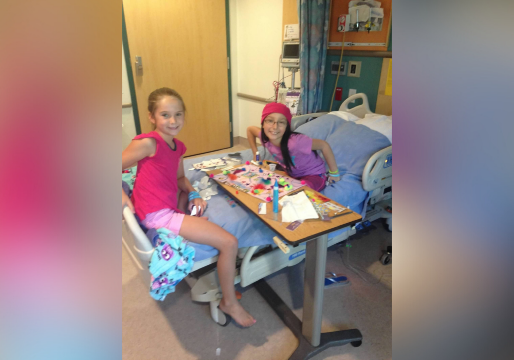 Mia and friend chatting in hospital bed.