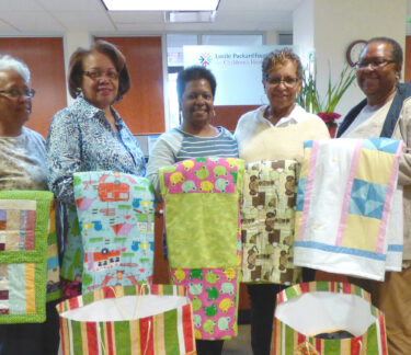 A group of volunteers hold up quilts they made