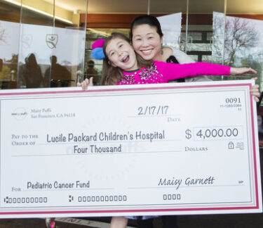 A young girl and her mother hold an oversized check showing the money she raised for the children's hospital