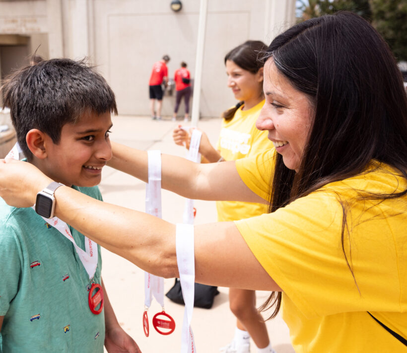 A volunteer hangs a medal on a young person at Summer Scamper